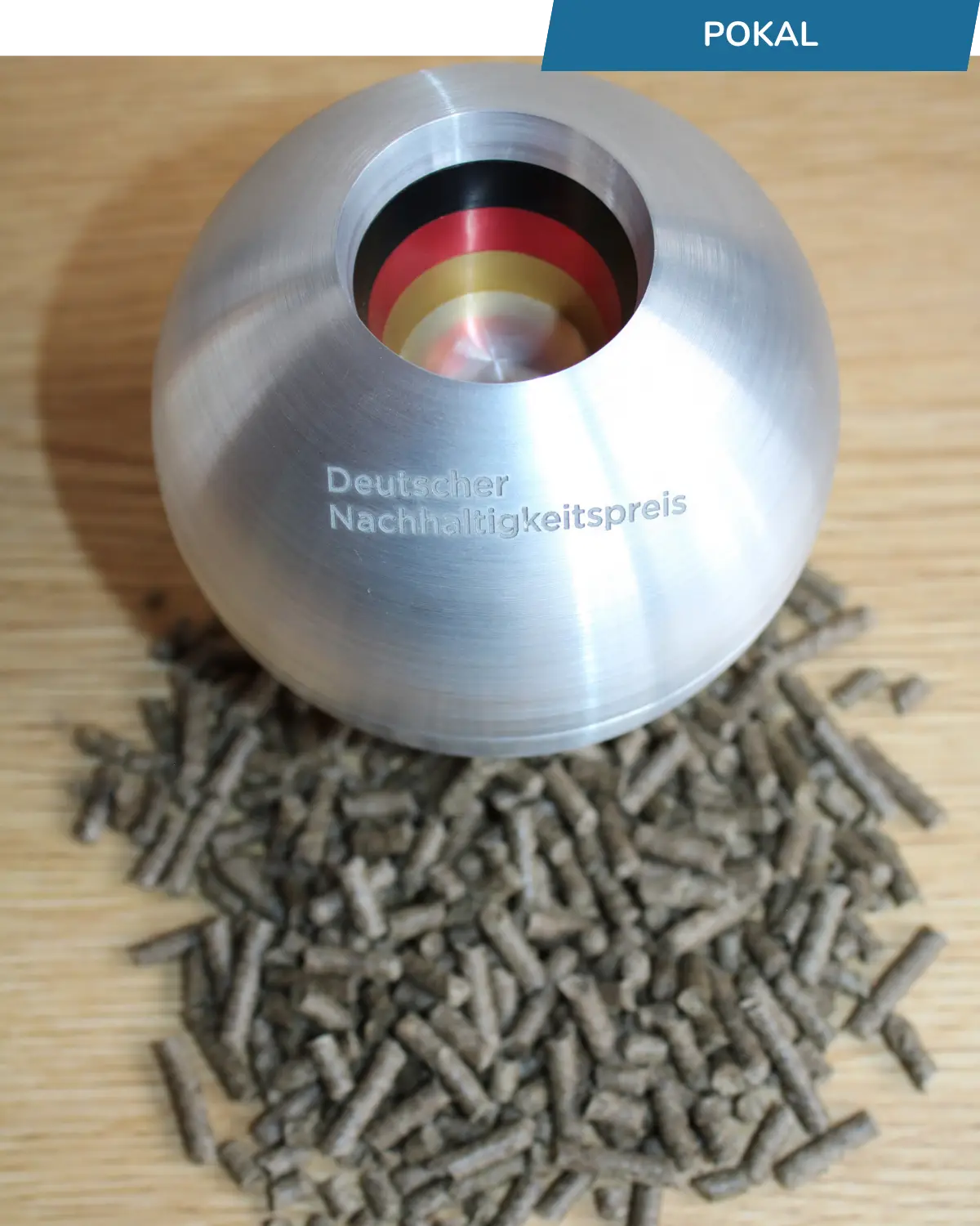 Ein kugelrunder Pokal mit der Aufschrift: Deutscher Nachhaltigkeitspreis. Davor Schafwollpellets.